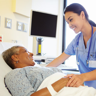 A medical professional catring for a patient laid in bed, both smiling at each other.