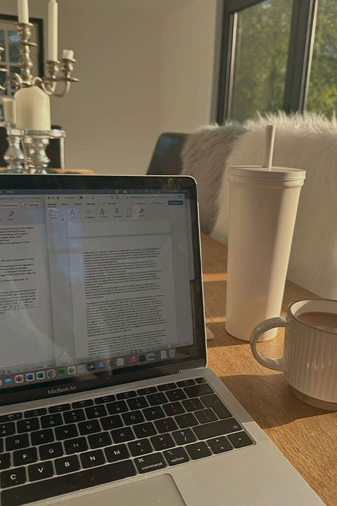 A laptop and cup on a dining room table.