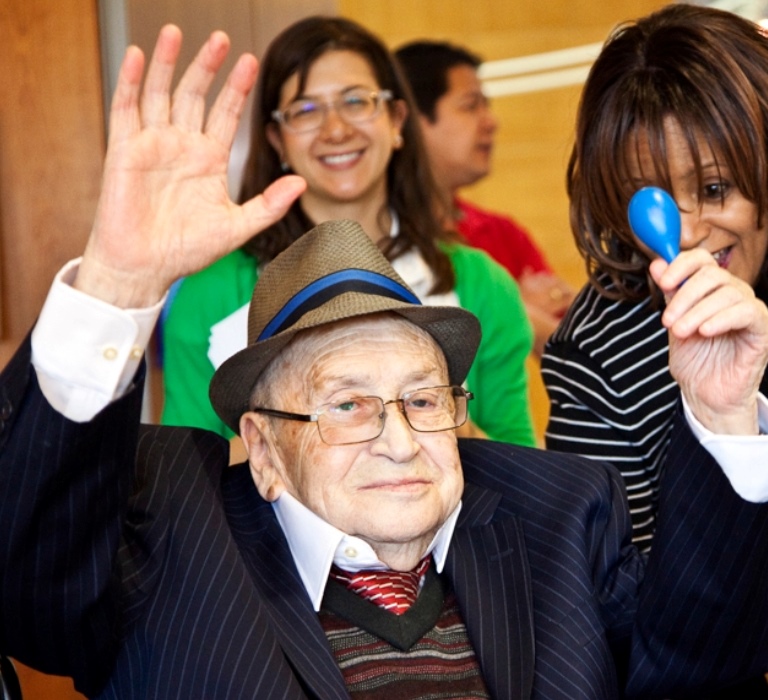An image of an elderly man celebrating and holding a balloon with people smiling around him