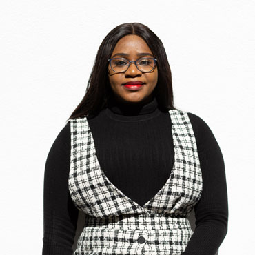 A student standing in front of a bright white wall, smiling at the camera