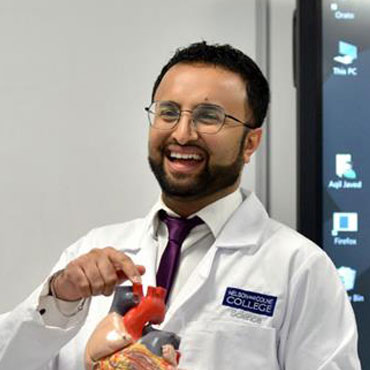 A student holding a model of a heart and smiling at the front of a classroom