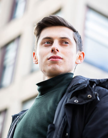 A student standing in front of a building and looking into the distance