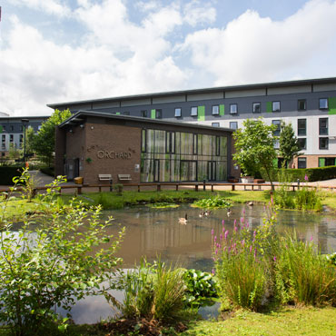 Three residential buildings of various heights with a pond in the foreground