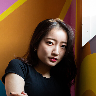 A postgraduate student posing in a colourful room on campus