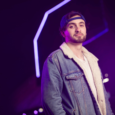 Student wearing a cap and denim jacket stood in front of purple lights