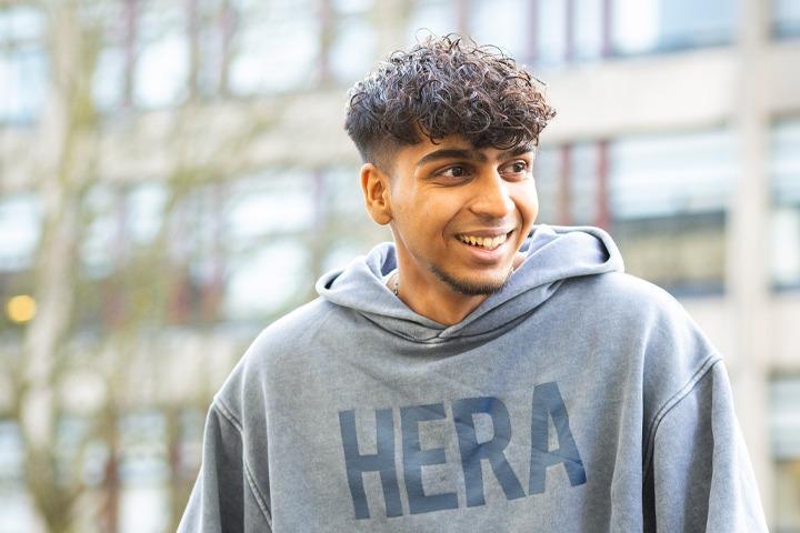 Student sat on a wall, wearing a hoodie, smiling
