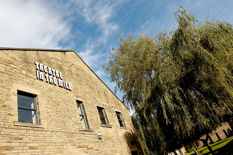 The exterior of a brick building with lettering on the wall that says Theatre in the Mill.