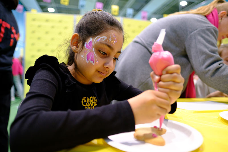 A young girl with her face painted decorating a cookie - part of UNIfy Festival 2024