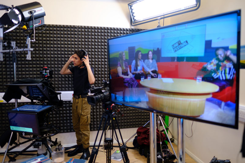 Behind the scenes in the TV studio showing a student filming the panel - Four panellists sat in the University's TV studio - part of UNIfy Festival 2024