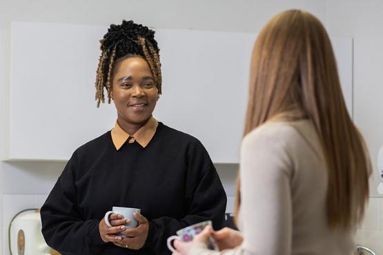 Two people stood talking in a kitchen whilst holding mugs