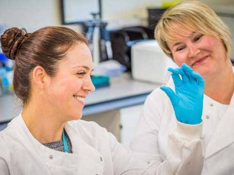 Two researchers smiling. One is holding a vial.