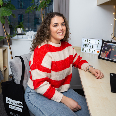 Smiling student sitting at a desk in their room.