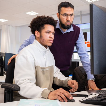 An academic member of staff watching a student at a computer.