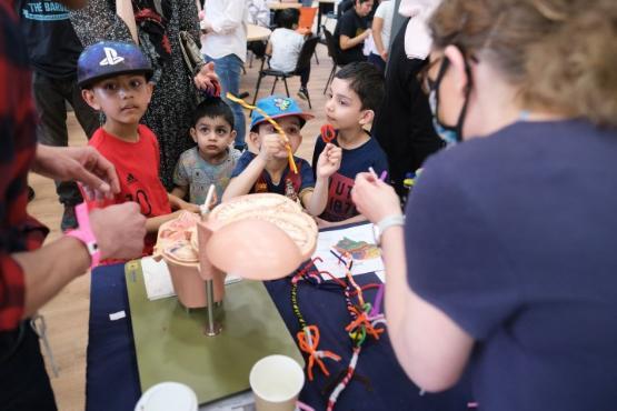 A group of four children stood behind a table look at a demonstration at a community day