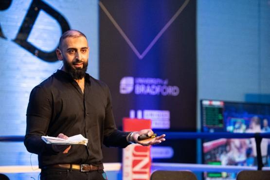 An academic stood up inside a boxing ring with a microphone around their face gives a presentation