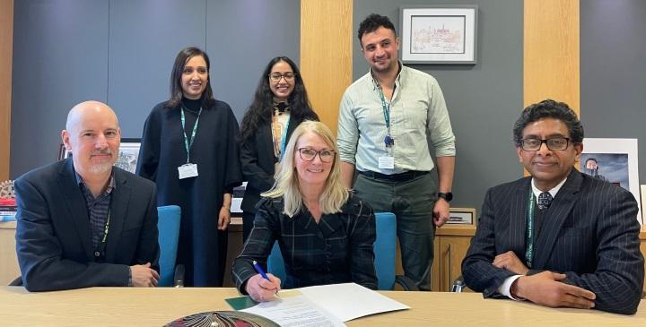 University staff sat down behind a table and a few other staff members stood up behind them for contract signing