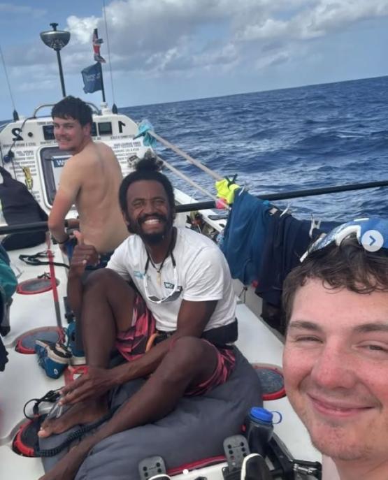 Three people on a boat in the middle of the ocean smiling at the camera