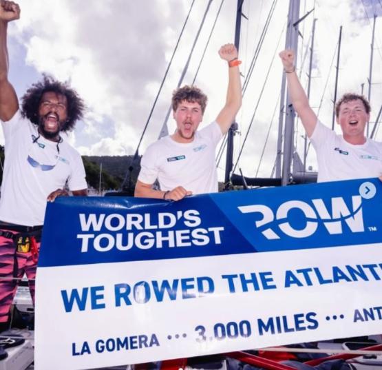 Three graduates stood next to each other on boat hold arms up to celebrate holding large sign in front of them