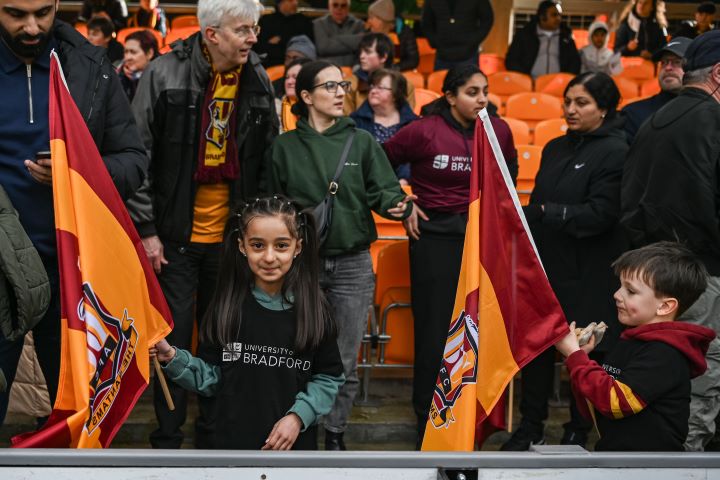 Children hold claret and amber flags in a football stand at a match