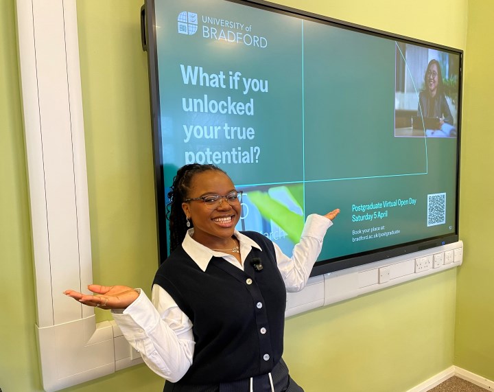 A person smiles with their arms held out to their side in front of video screen