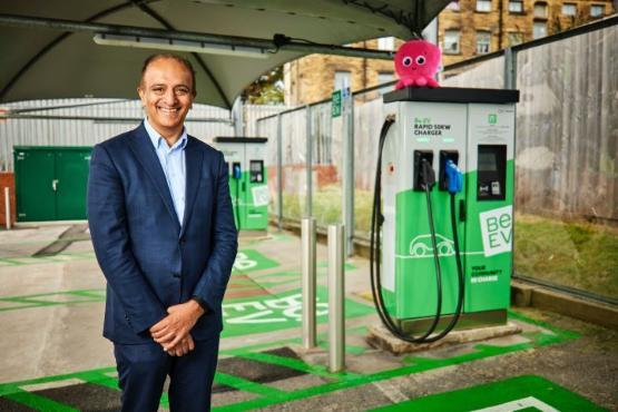 A person dressed in a suit stands next to an electric vehicle charging point