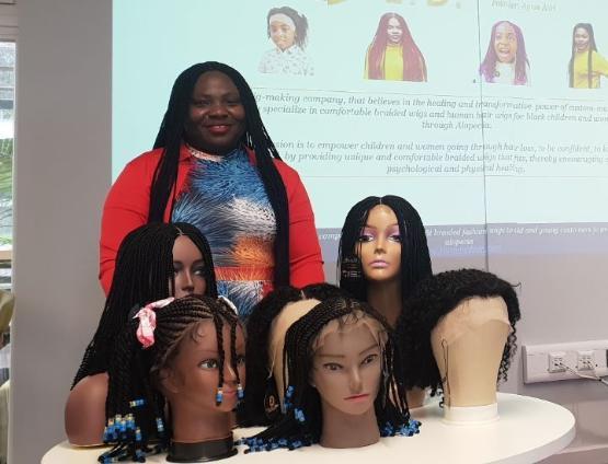 A person stands behind a table filled with six mannequin heads which are all wearing wigs