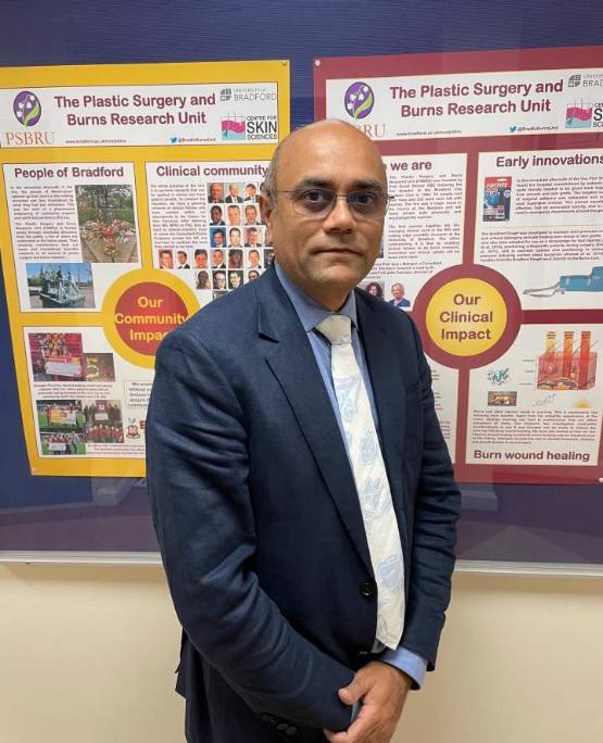 A person dressed in a suit and tie stands in front of two brightly coloured posters on a wall