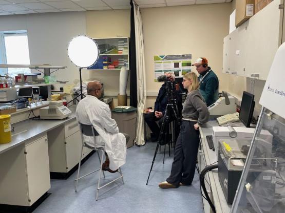 An academic dressed in a white lab coat is interviewed