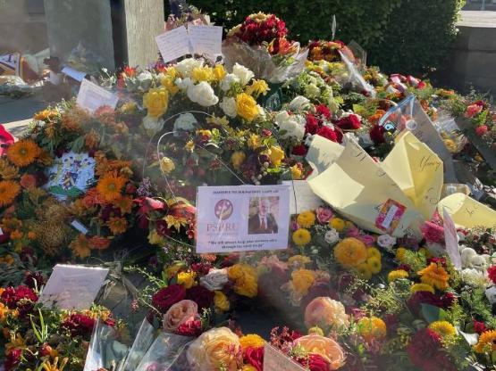 A close-up of a card left on a floral tribute as part of a larger collection of flowers