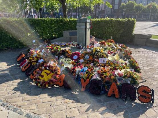 a shaft of sunlight illuminates a collection of floral tribute left at a monument