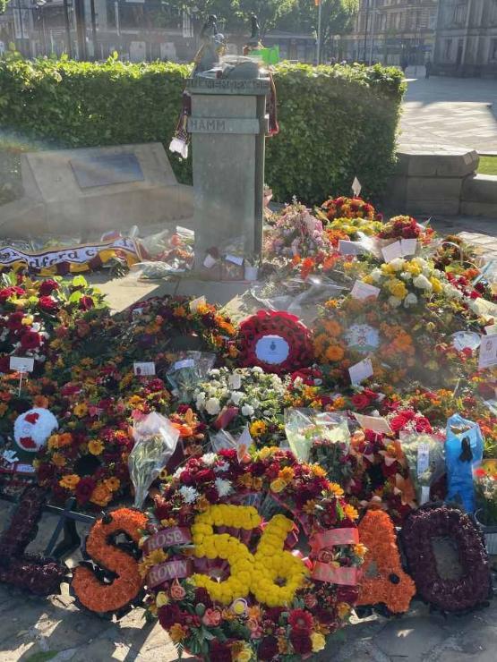 A stone monument with lots of colourful floral tributes in front of it