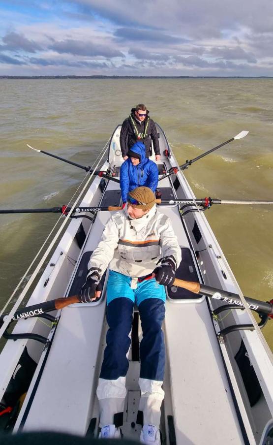 Two people sat behind each other row on a boat