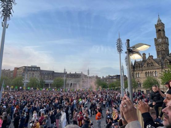 A huge crowd gather in a public space for a celebration with blue sky