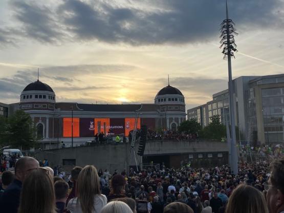 A huge celebration event held in a public place with a large video screen behind with claret and amber stripes on it