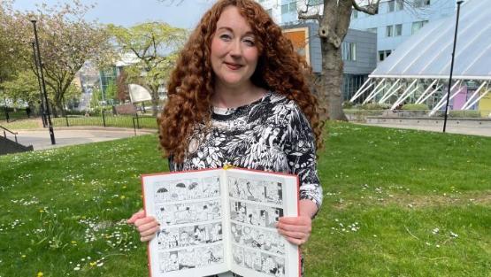 An academic holds up an open comic book