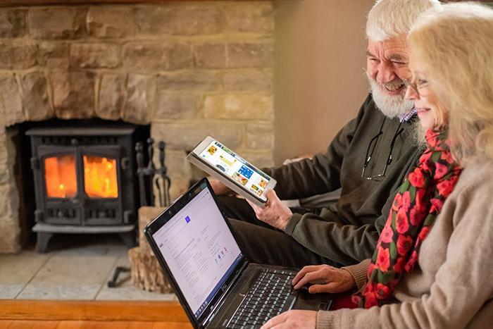 An older couple sat next to each other looking at a laptop and tablet