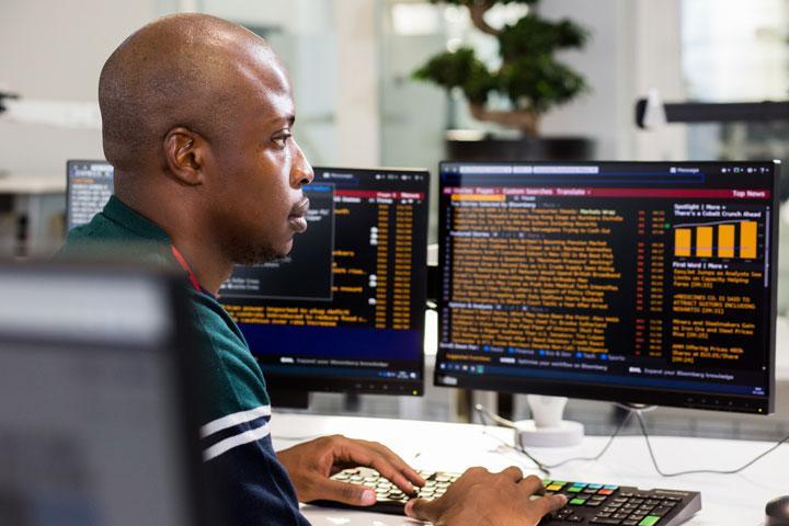 A person sitting at a desk typing on a computer keyboard and looking at two computer monitors. 