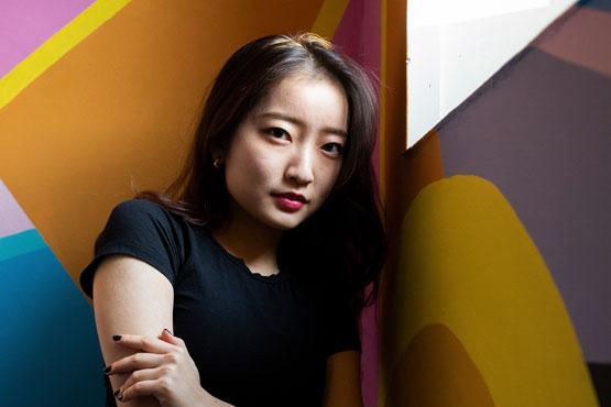 A student looking at the camera leaning on a colourful wall.