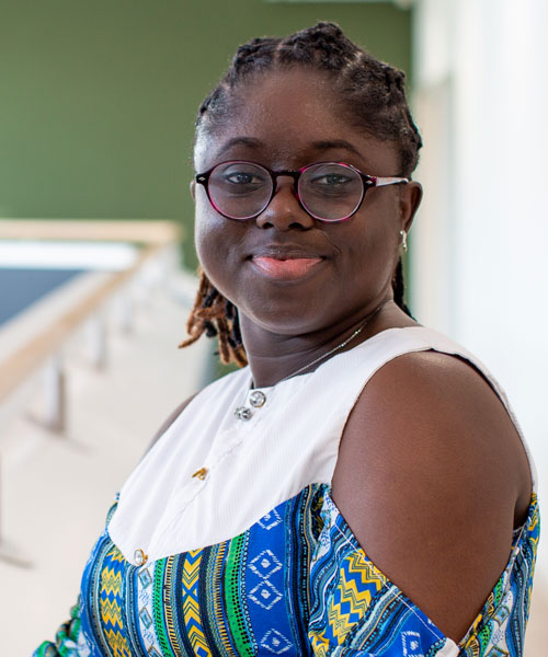 A person leaning on a railing, smiling at the camera in a well-lit indoor space.