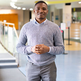 A smartly dressed person standing in large, brightly lit classroom.