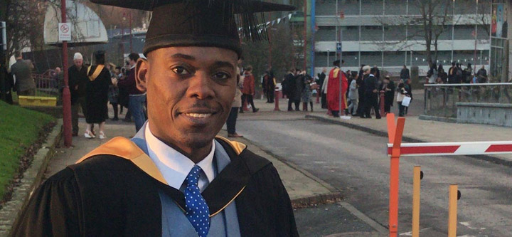 Billy Chabalenge wearing graduation attire, standing outside with several graduates in the background