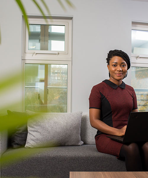 Smiling student sat on a sofa with a laptop